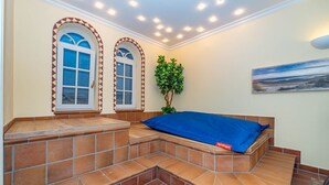 Una habitación con un banco empotrado, dos ventanas en arco, una planta en maceta y un cuadro en la pared.