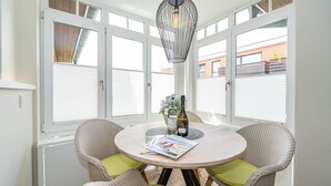 Une table ronde, deux chaises en osier, un magazine et deux bouteilles d’alcool.