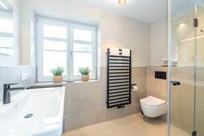 A modern bathroom with a large white bathtub, a glass shower enclosure, and a toilet.