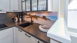 Una cocina con encimera negra, armarios blancos, un lavabo y una escena decorativa de playa en la pared.