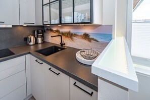 Una cocina con encimera negra, armarios blancos, un lavabo y una escena decorativa de playa en la pared.
