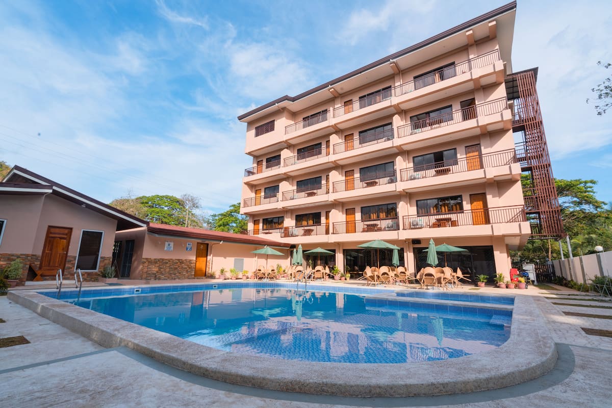 A multi-story hotel with a swimming pool, outdoor seating, and balconies.