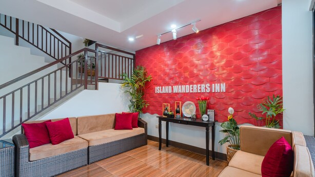 A lobby with a red textured wall, a staircase, wicker sofas with red cushions, and a table with a sign. - Island Wanderers Inn (Coron)