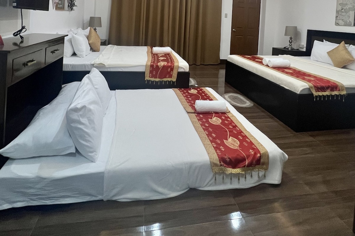 A hotel room with two beds, a desk, a TV, and a ceiling light.