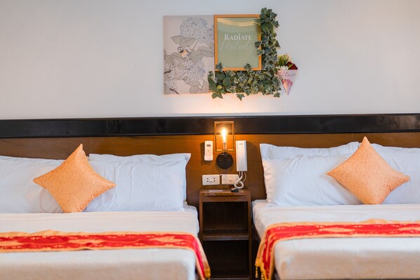 Habitación de hotel con dos camas, ropa de cama blanca, cabecera de madera, teléfono en la pared y un cuadro con una planta.