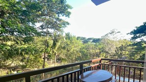 Un balcón con una mesa y dos sillas, con vistas a un jardín exuberante y un estacionamiento.