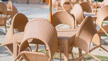 Wicker chairs and tables arranged outdoors with green umbrellas.