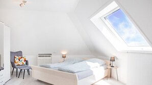 Makuuhuone, jossa on kalteva katto, kattovalokuvio, sänky, tuoli, yöpöytä ja lamppu.