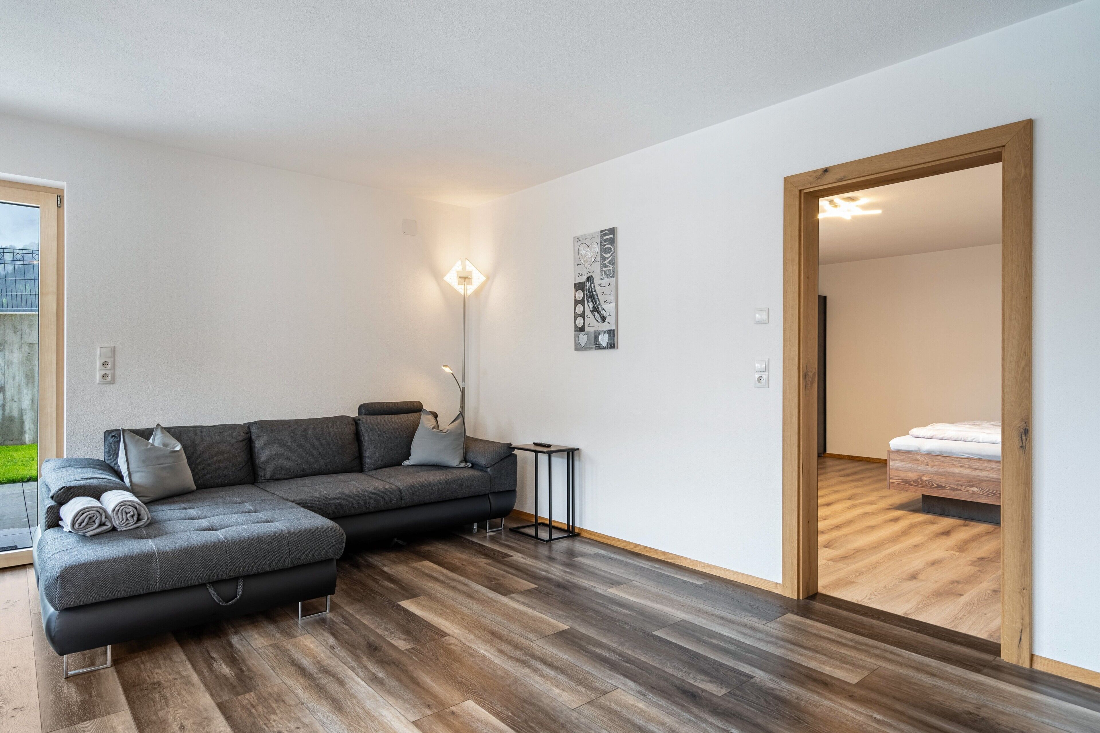 A modern living room with a sectional sofa, a small side table, and a wooden floor.