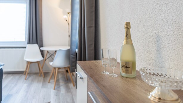 Una habitación con una mesa de madera, una botella de Freixenet, dos copas y un cuenco de vidrio.