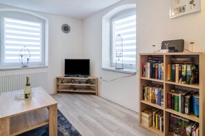 Un salon équipé d’un téléviseur, d’une bibliothèque et de deux fenêtres avec des stores.