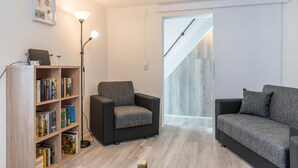 Una sala de estar con una estantería, dos sofás, una lámpara de pie y una escalera.