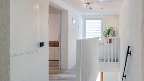 Un pasillo con una puerta blanca, una escalera y una cocina al fondo.