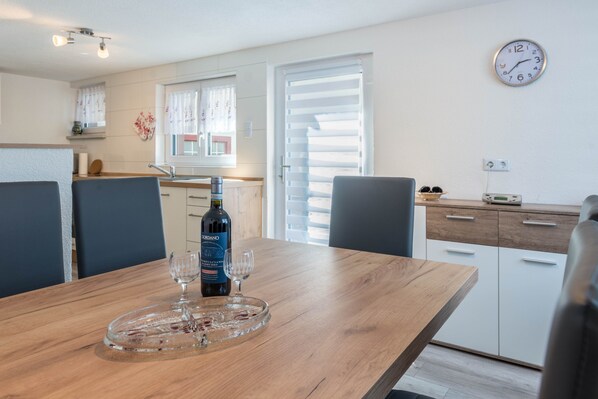 Un coin repas avec une table en bois, deux chaises, une bouteille de vin et deux verres à vin.