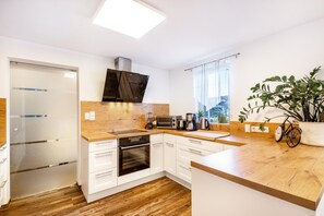 A modern kitchen with white cabinets, wooden countertops, a built-in oven, a microwave, and a coffee maker.