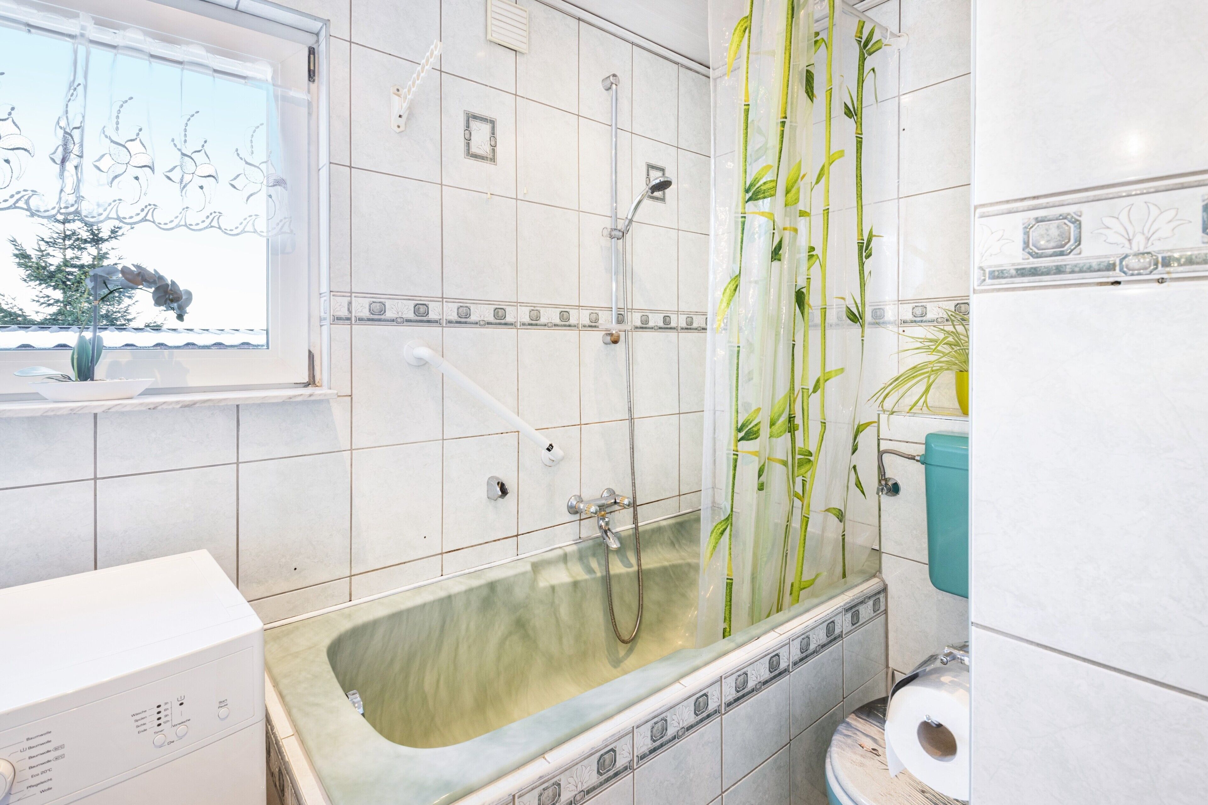 A bathroom with a bathtub, toilet, and window with a plant.