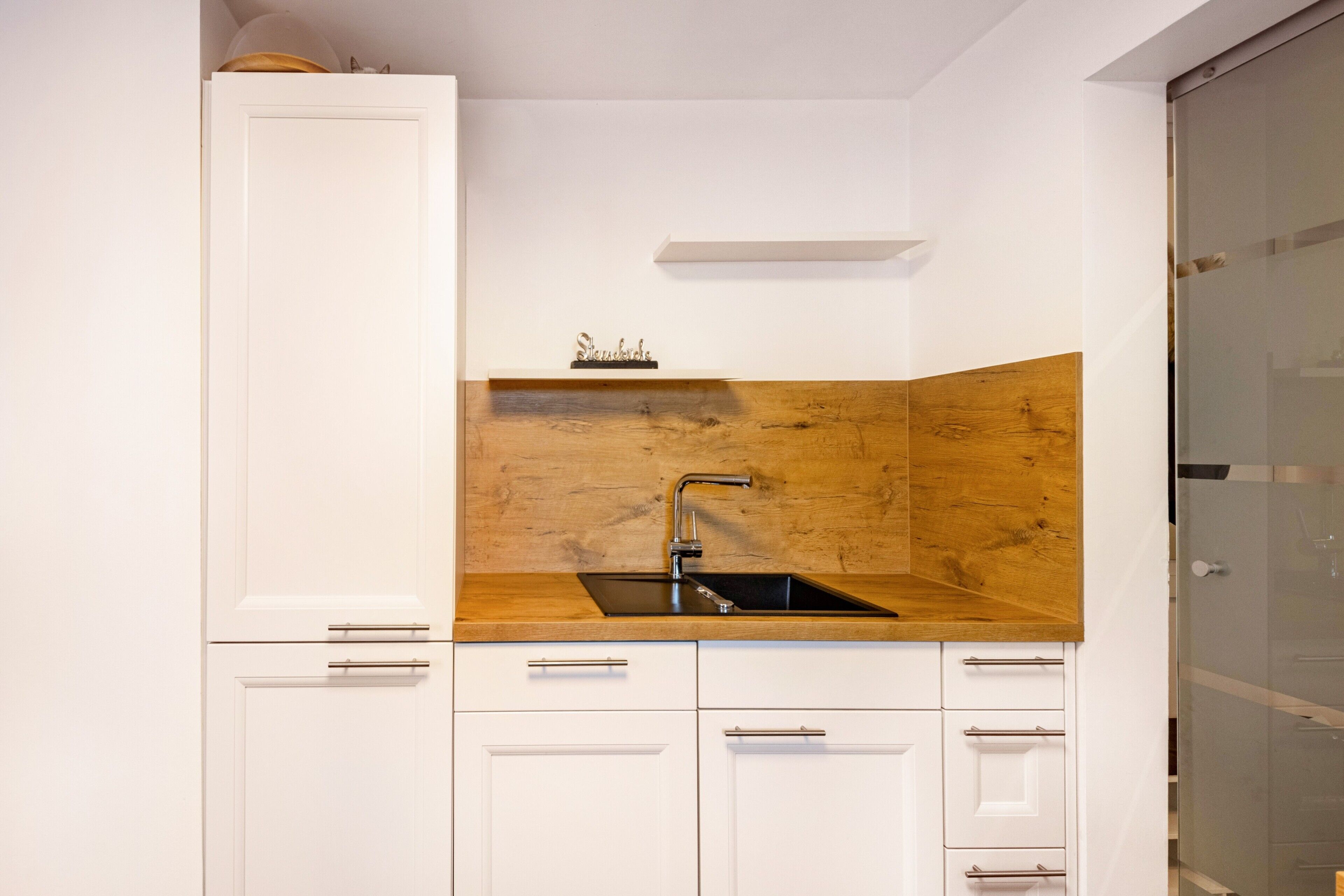 Una cocina con armarios blancos, protector contra salpicaduras de madera y un lavamanos de acero inoxidable.