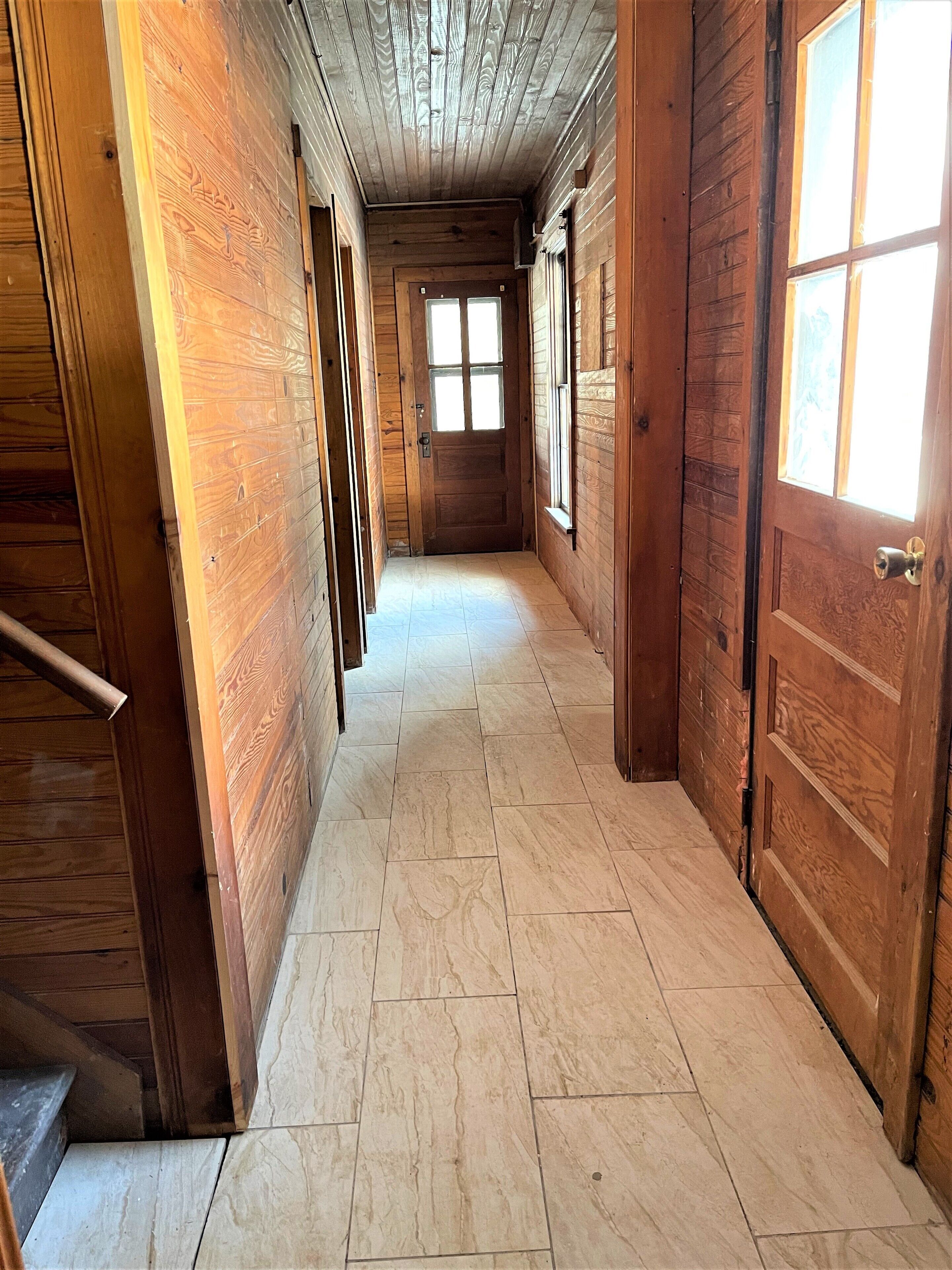 Un couloir en bois, avec un sol carrelé, des portes en bois et des fenêtres.