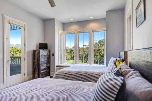 Ein Schlafzimmer mit einem großen Bett, einem Fernseher und Blick auf Grünflächen durch das Fenster.