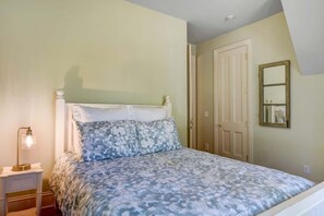 Ein Schlafzimmer mit Bett, Nachttisch, Lampe und einer Tür.