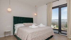 Ein Schlafzimmer mit einem großen Bett, Blick ins Freie durch eine Schiebetür und einem kleinen Nachttisch.