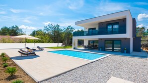 Ein modernes, zweistöckiges Haus mit Swimmingpool, Sitzgelegenheiten im Freien und einem gepflegten Garten.
