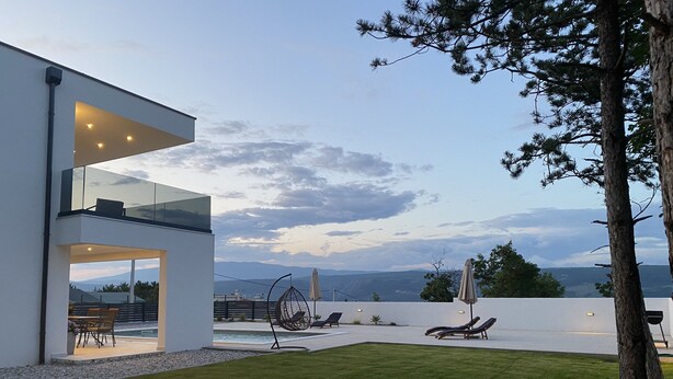 Ein modernes Haus mit einem Glasbalkon mit Blick auf ein Schwimmbad und Berge.