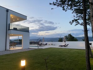 Una casa moderna con un balcone in vetro affacciato su una piscina e montagne.