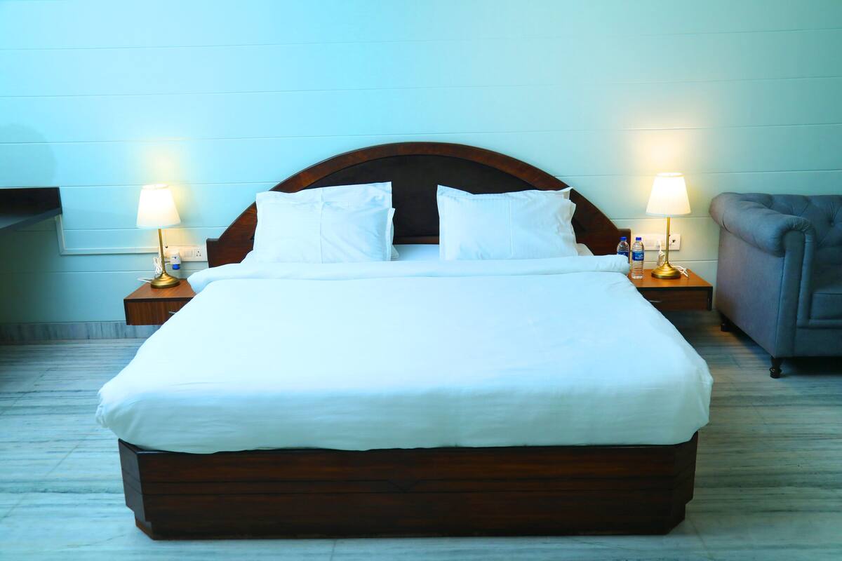 A neatly made bed with white linens, two bedside tables with lamps, and a grey upholstered armchair.