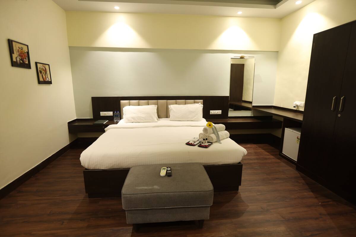 A neatly arranged bedroom with a large bed, a bedside table, a small ottoman, a mirror, and a wardrobe.