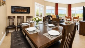 A dining area with a long wooden table, multiple chairs, a fireplace, and large windows. - Gigantic 6b5b home with stunning view & spacious rooms (Fairbanks)