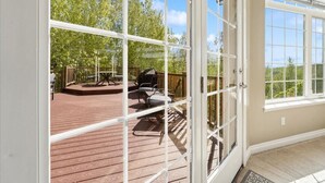 A view through a glass door to an outdoor deck with a barbecue grill, chairs, and a table. - Gigantic 6b5b home with stunning view & spacious rooms (Fairbanks)