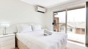 Een slaapkamer met een groot bed, een nachtkastje, een lamp en een schuifdeur naar een balkon.