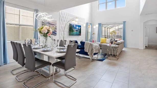 Ein geräumiger Wohnbereich mit Esstisch für vier Personen, einem blauen Sofa und einem großen Fenster mit Jalousien.