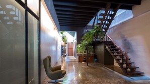 A narrow corridor with a modern chair, a staircase, and potted plants. - The Urban Room (Phuket)