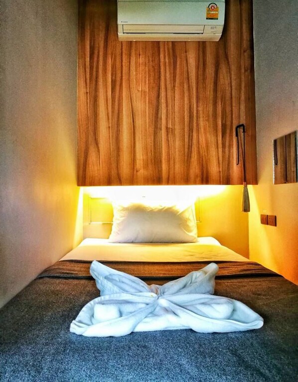 Una camera d'albergo con un letto, una testata in legno, un condizionatore d'aria e un asciugamano sul pavimento.