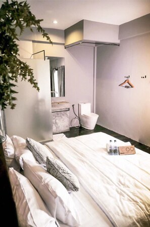 A modern hotel room with a large bed, a small bathroom, and a plant. - The Urban Room (Phuket)
