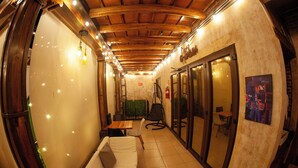 A narrow corridor with a wooden ceiling, a white sofa, and a small table with a cushion. There are chairs and a green wall in the background.