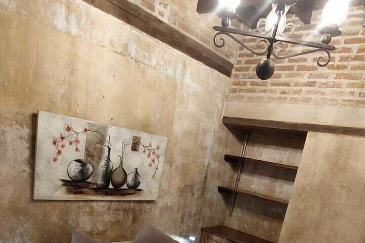 A bedroom with a bed, a painting on the wall, and a wooden ceiling structure.