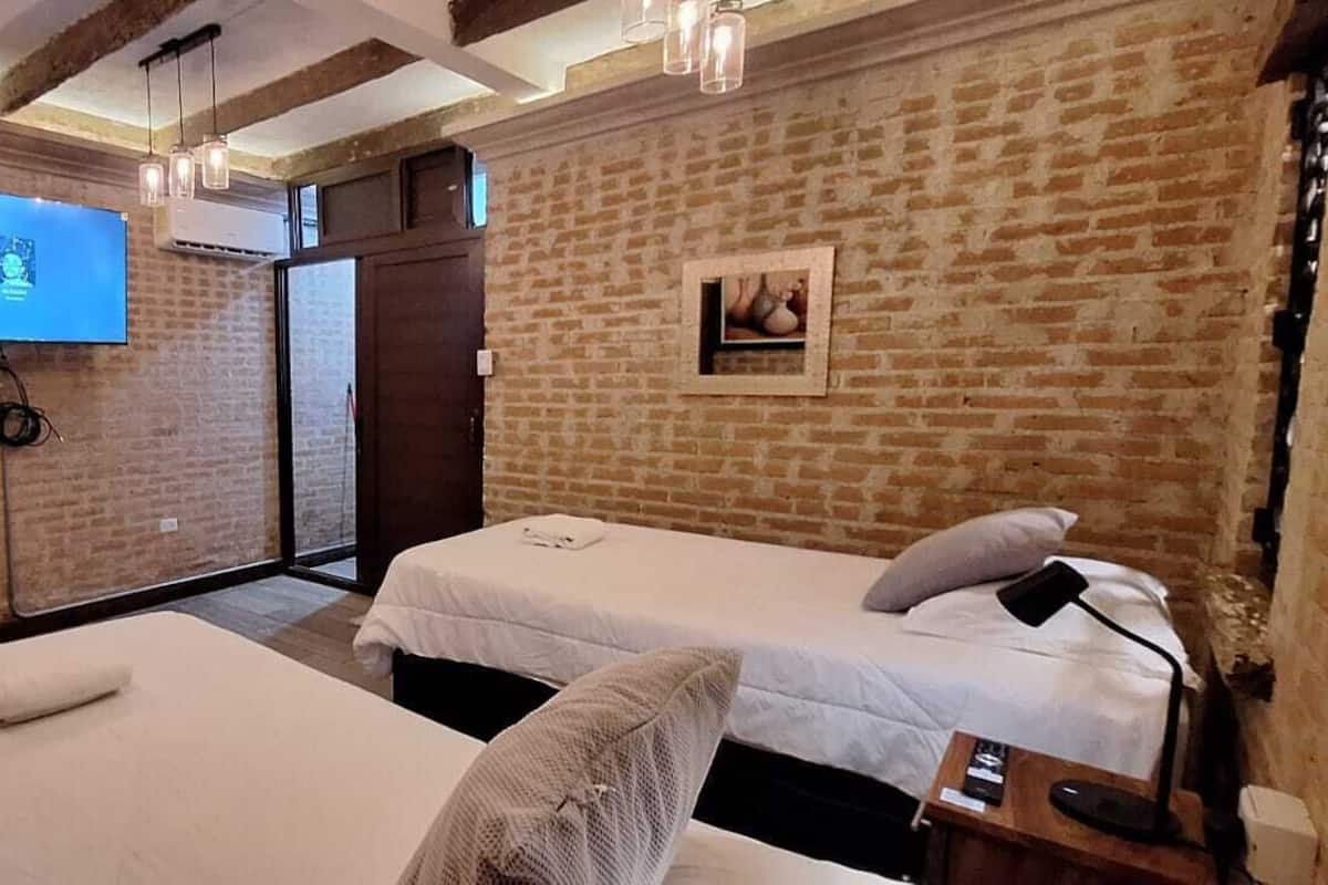 A hotel room with two beds, a TV mounted on the wall, and a brick wall.