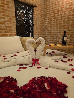 A hotel room with a brick wall, a decorative metal gate, a bed with rose petals, a bottle of wine, and glasses on a side table. - Hot Chipilin  (Antigua Guatemala)