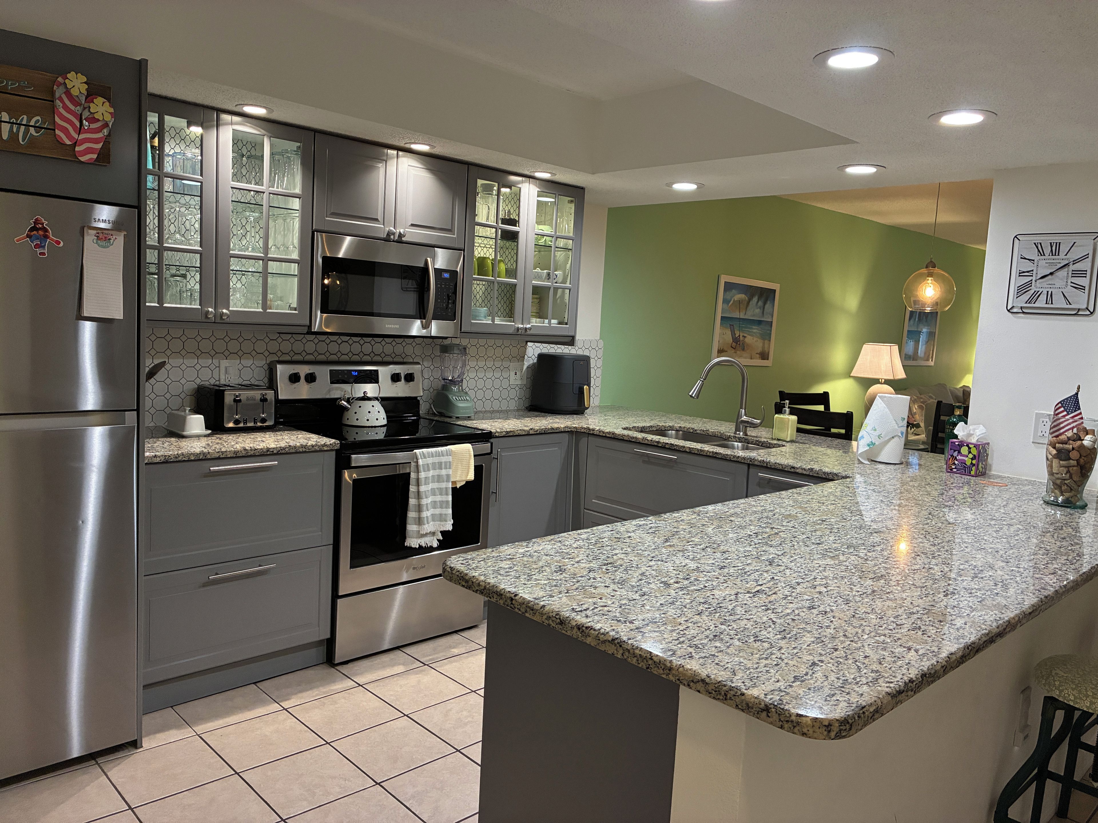 A modern kitchen with stainless steel appliances, a granite countertop, and a green accent wall.