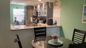 Una cocina moderna con comedor, que incluye una mesa redonda con sillas, una lámpara colgante y vista al salón.