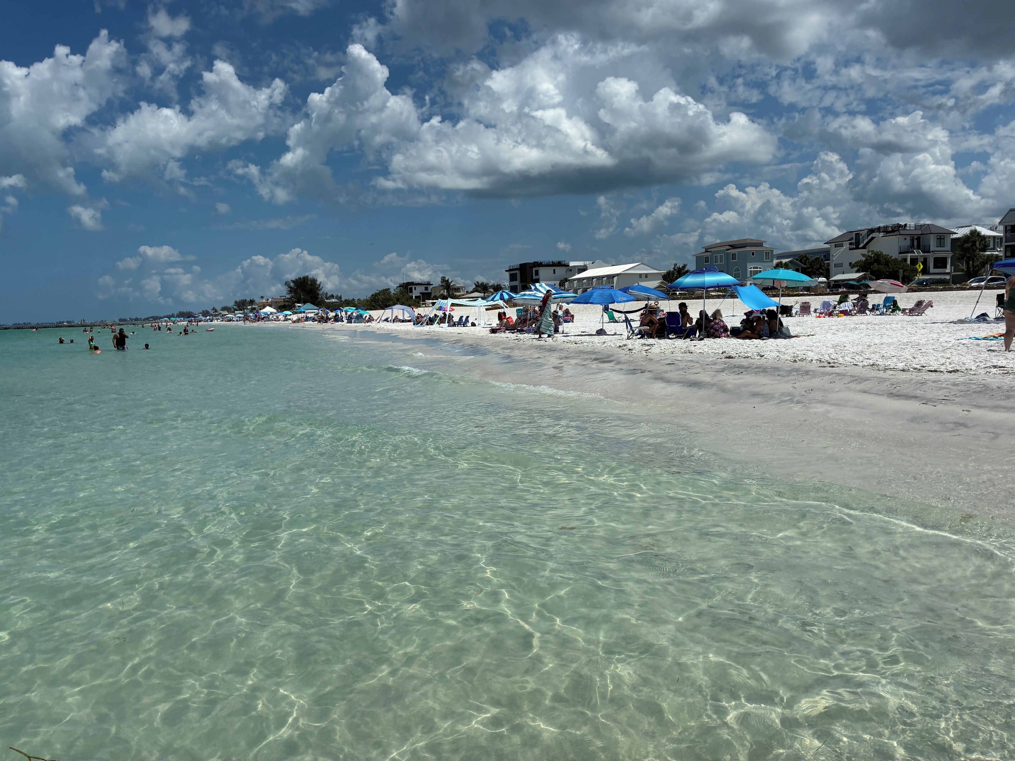 A beach with clear water, umbrellas, and beachgoers.