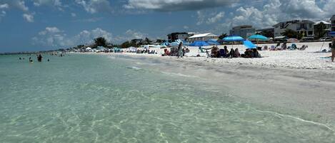 A beach with clear water, umbrellas, and beachgoers.