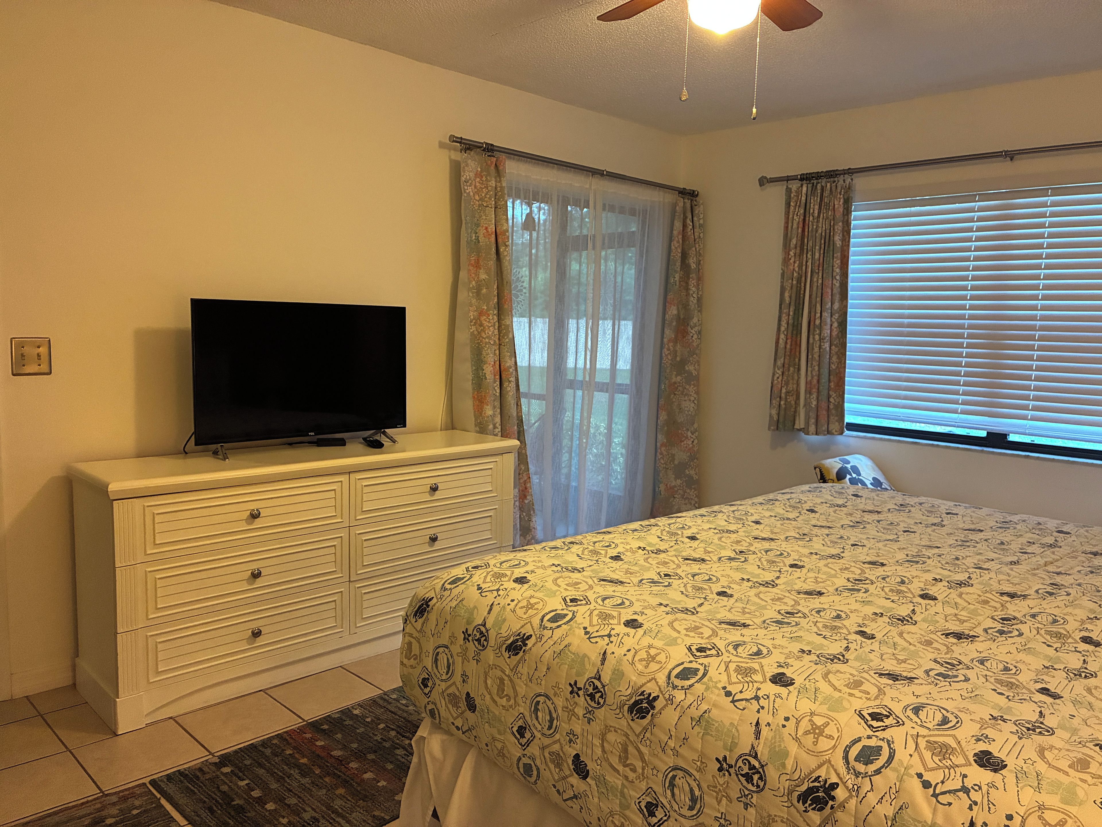 Un dormitorio con cama, cómoda, televisor y ventana con persianas.