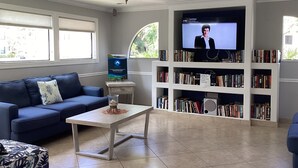 Una sala de estar con un sofá azul, una mesa de centro, un televisor y una estantería llena de libros.