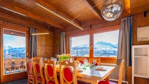 Ein Esszimmer mit Holzboden, einem Tisch für sechs Personen, großen Fenstern mit Bergblick und einer Discokugel an der Decke.