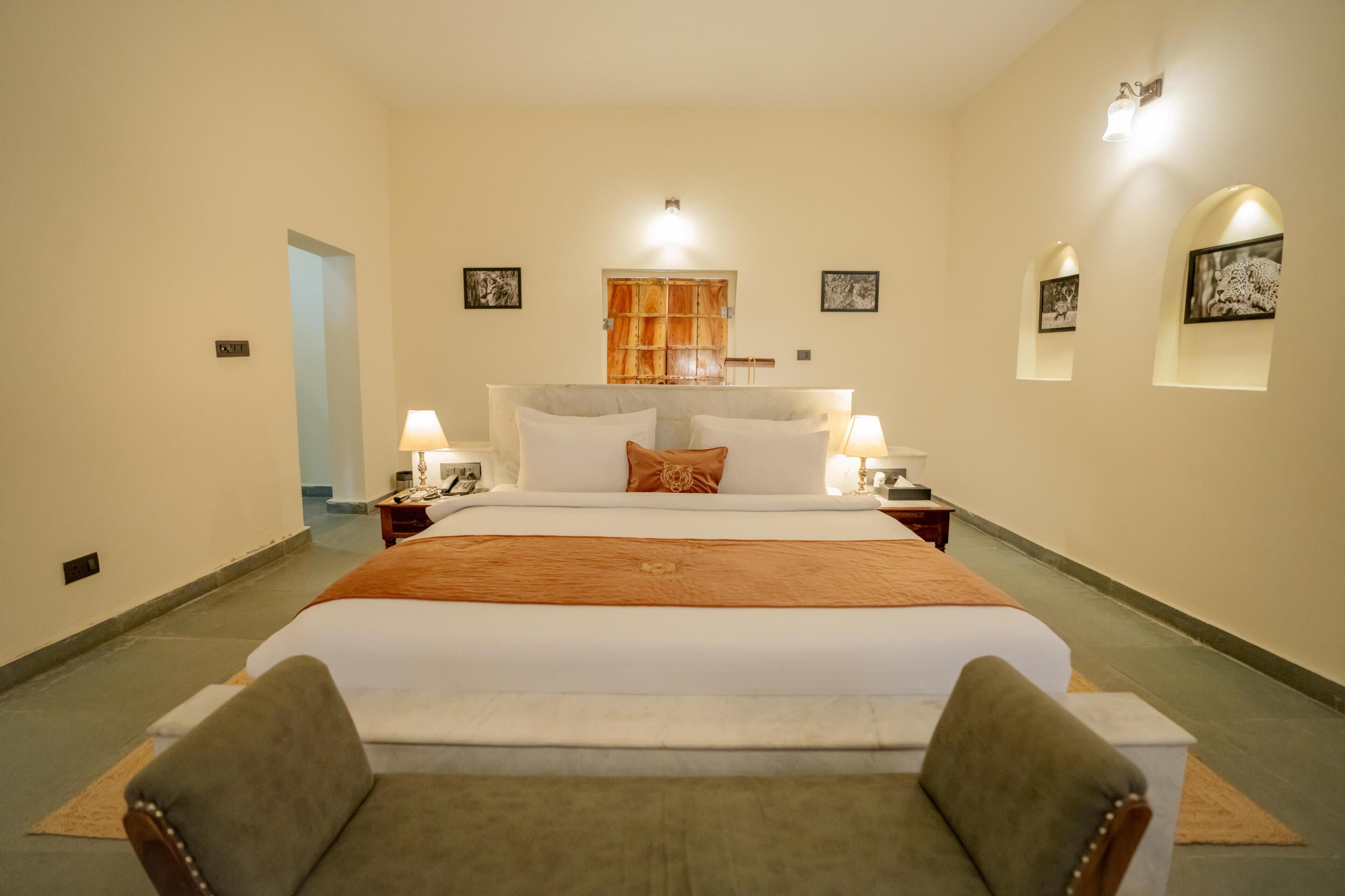 A hotel room with a large bed, two bedside tables, a nightstand, a sofa, and a door leading to another room.
