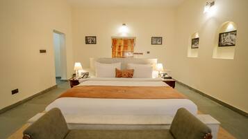 A hotel room with a large bed, two bedside tables, a nightstand, a sofa, and a door leading to another room.